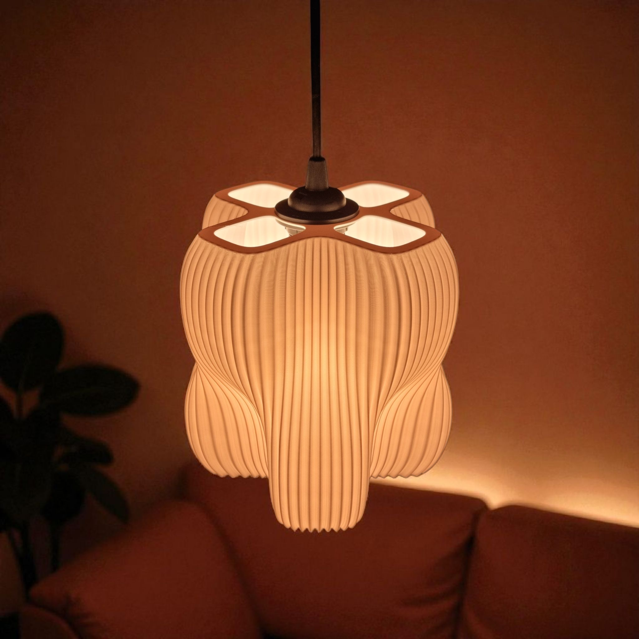 A pendant lamp with a sculptural design featuring four lobes and a finely striated surface is illuminated, casting a warm glow in a cozy setting. The soft light enhances the organic shape, creating an inviting atmosphere.