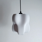 A modern pendant lamp features a sculptural design with a textured, pleated white surface and an organic shape made up of four lobes. It hangs from a black cord against a simple gray background, creating a striking focal point.