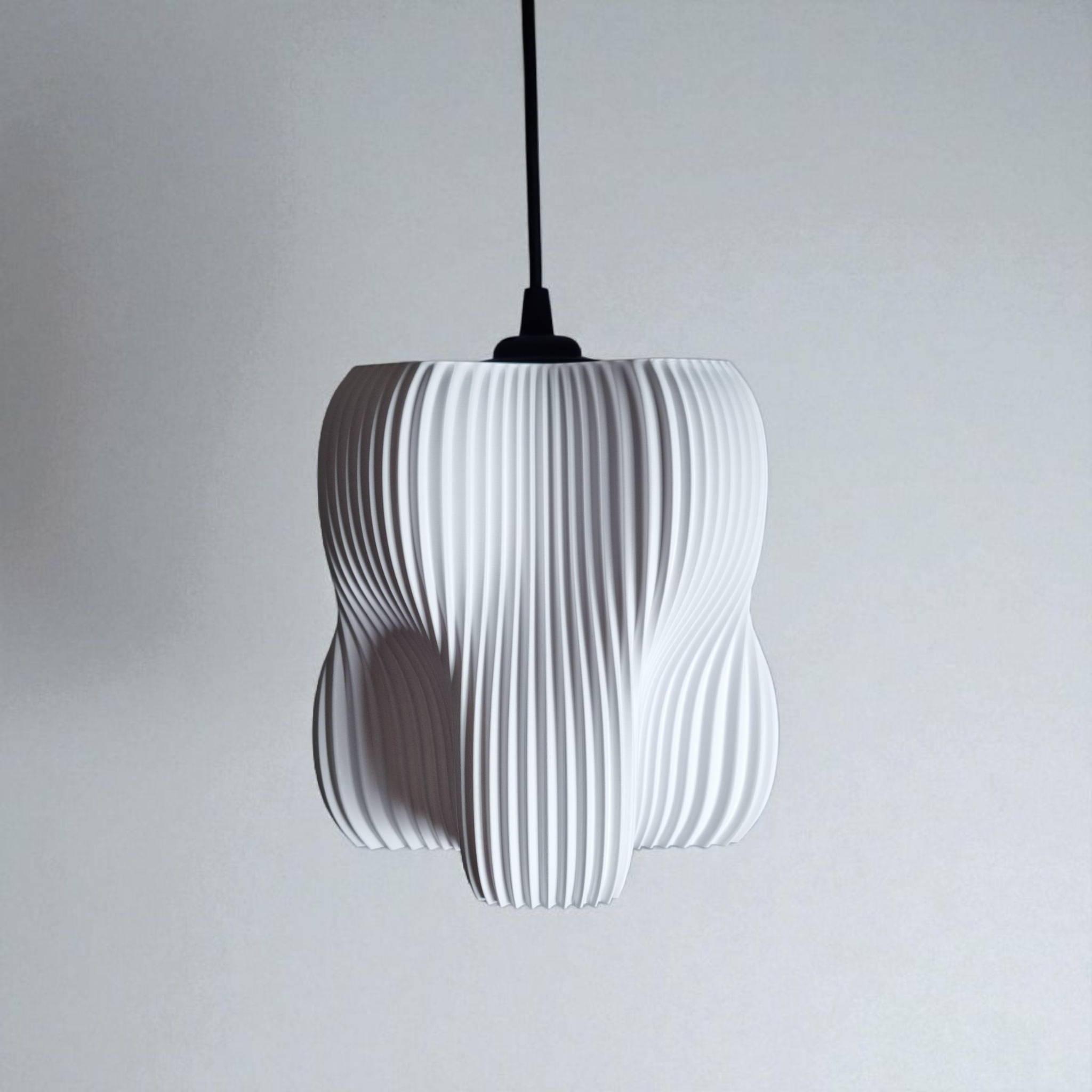 A modern pendant lamp features a sculptural design with a textured, pleated white surface and an organic shape made up of four lobes. It hangs from a black cord against a simple gray background, creating a striking focal point.