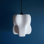 A sculptural white pendant lamp with a textured, pleated design hangs against a deep blue wall. Its organic shape features four lobes, creating a soft diffusion of light that enhances the overall ambiance of the space.