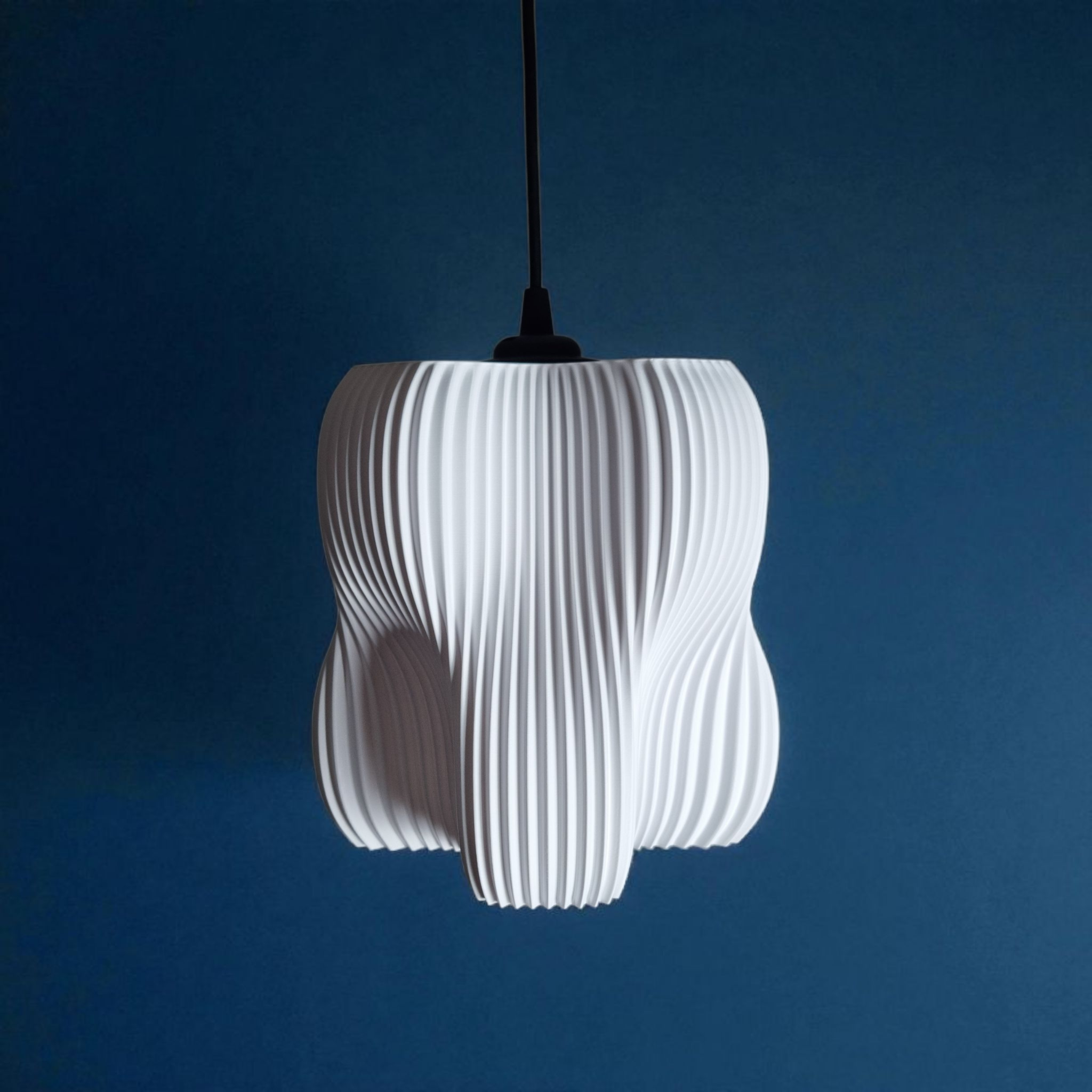 A sculptural white pendant lamp with a textured, pleated design hangs against a deep blue wall. Its organic shape features four lobes, creating a soft diffusion of light that enhances the overall ambiance of the space.
