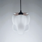 A pendant lamp with a sculptural design featuring an organic, four-lobed shape and a finely striated white surface that diffuses light softly. It hangs from a black cord against a neutral backdrop, creating a modern focal point.