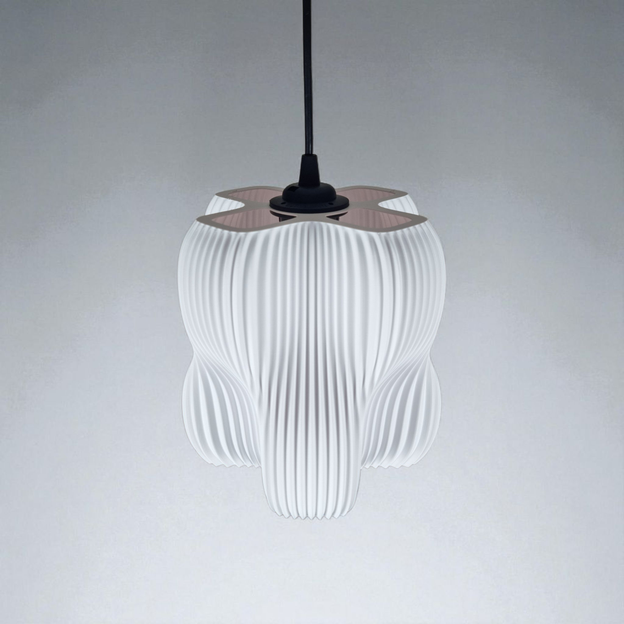 A pendant lamp with a sculptural design featuring an organic, four-lobed shape and a finely striated white surface that diffuses light softly. It hangs from a black cord against a neutral backdrop, creating a modern focal point.