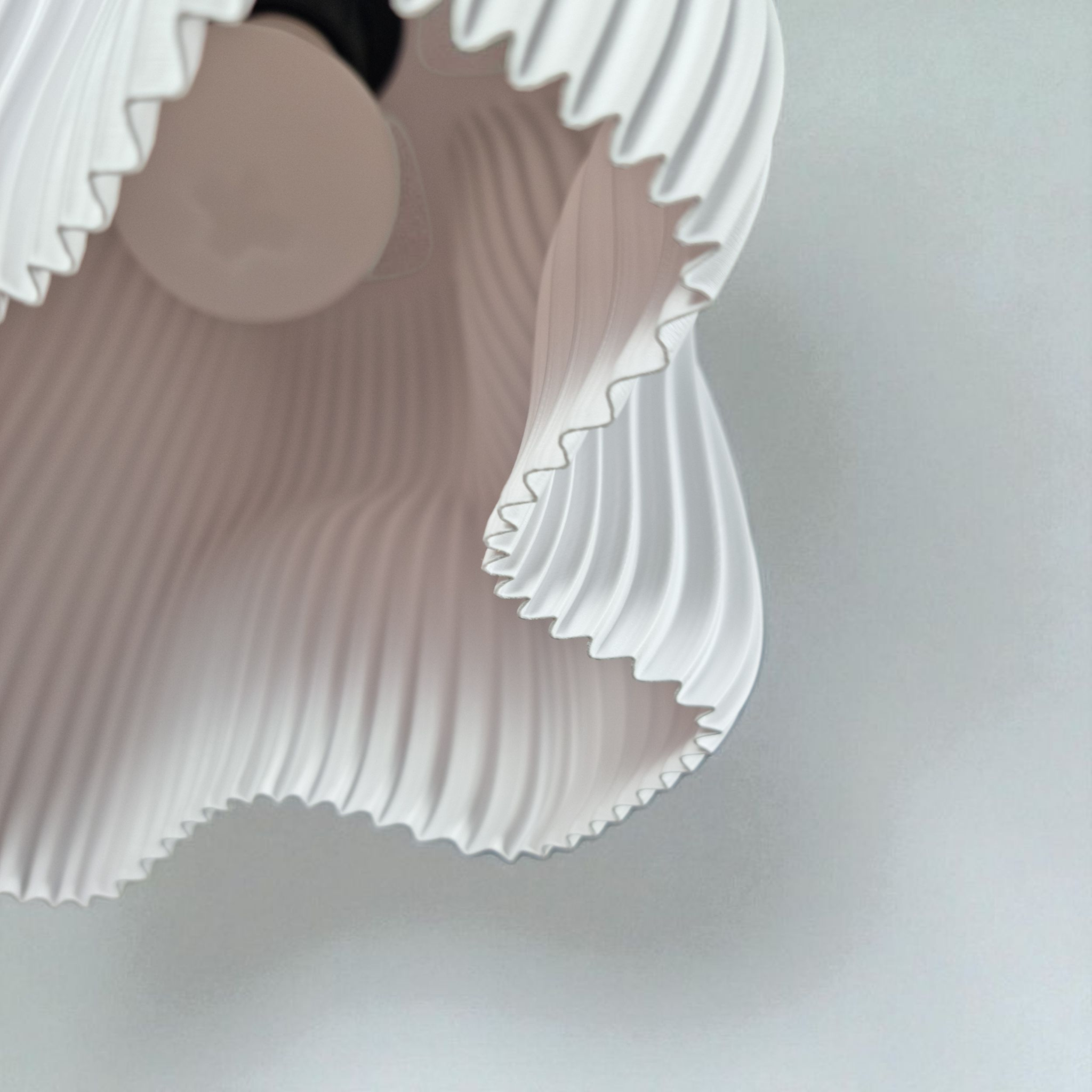 A close-up view of a white lamp shade with a wavy, pleated design, showcasing its organic shape and structured silhouette. The interior reveals a light bulb, enhancing the soft diffusion of light through the textured surface.