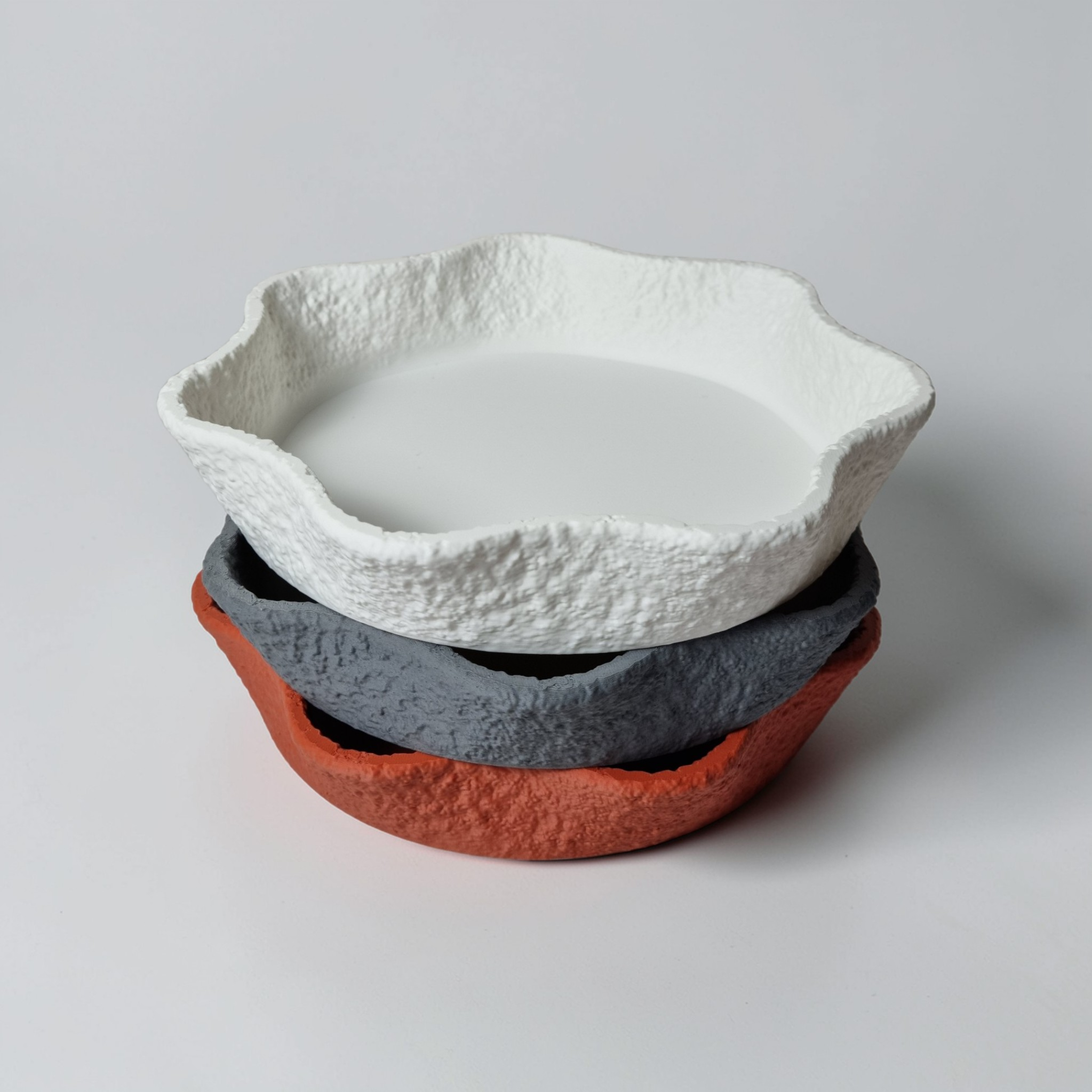 A set of three decorative bowls stacked together, featuring irregular, textured edges. The bowls are in white, gray, and terracotta colors, showcasing an organic design that contrasts smooth and rough surfaces, perfect for holding.