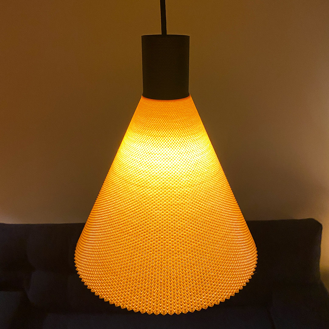 A modern pendant lamp with a conical shape features a textured orange shade that radiates a warm glow. The lamp hangs from a black ceiling fixture against a softly lit background, creating an inviting atmosphere in the space.