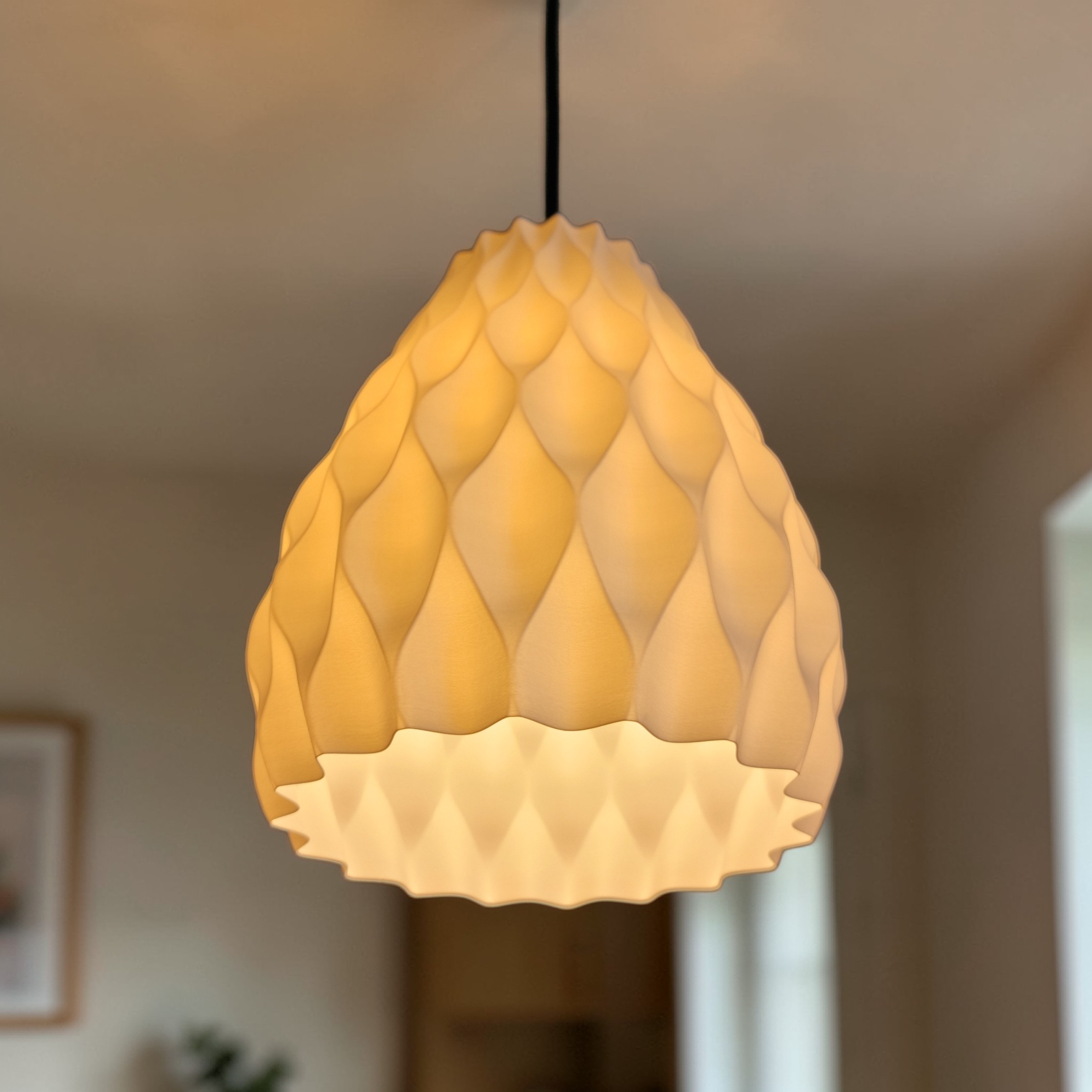 A textured pendant lamp with an organic, three-dimensional design hangs from a black cord. Its soft, warm light casts gentle shadows and highlights the intricate facets of the lamps surface, creating an inviting atmosphere.