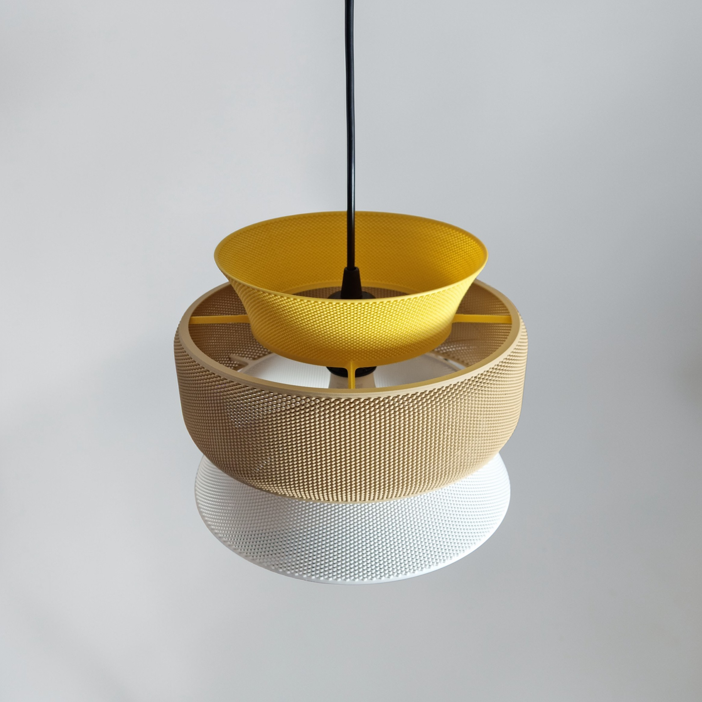 SAN pendant lamp, close-up view of its three stacked rings in textured bioplastic — mustard yellow, sand and white