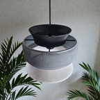 A modern pendant lamp features three interlocking mesh shades in black, gray, and white, creating a layered geometric design.