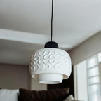 White sculptural pendant lamp SEAMLESS hanging above a sofa, close view of the organic pattern and layered drum silhouette