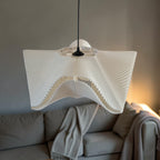 White SINE designer pendant light above a beige sofa, sculptural bioplastic lampshade for a japandi living room.