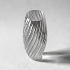 TEXTURIA Cristal vase in clear recyclable bioplastic, tilted angle with dramatic shadow, showing the full spiral silhouette and glass-effect transparency